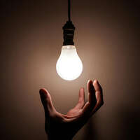 L'électricité symbolisée par une ampoule façonnée par l'homme avec une main en dessous.